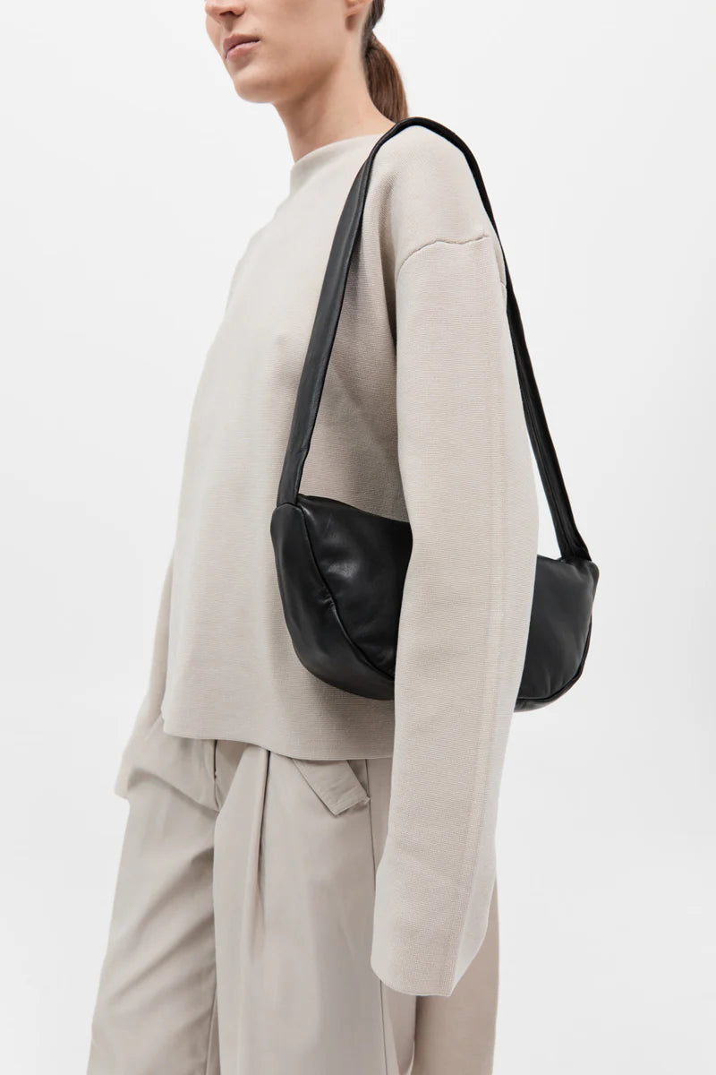 woman wearing a minimal beige outfit paired with a sleek crescent shaped banana bag in black leather 