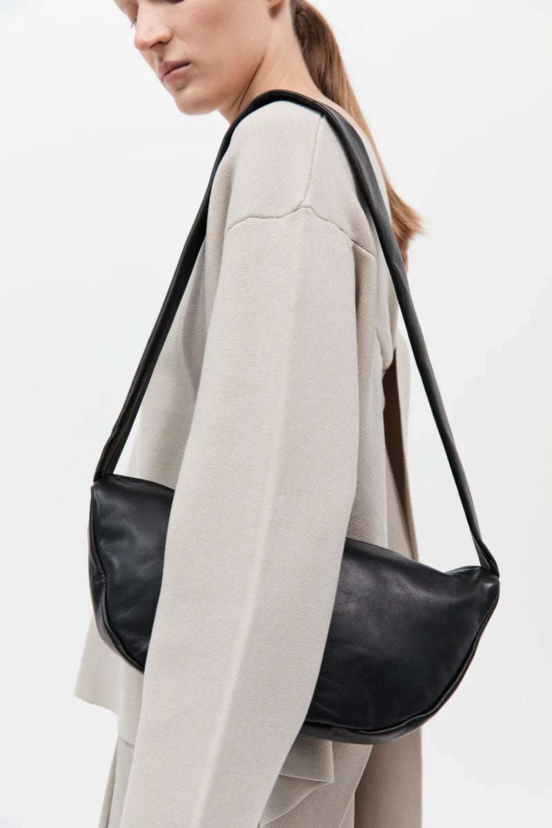 Woman wearing a minimal beige outfit and carrying a crescent shaped black leather handbag