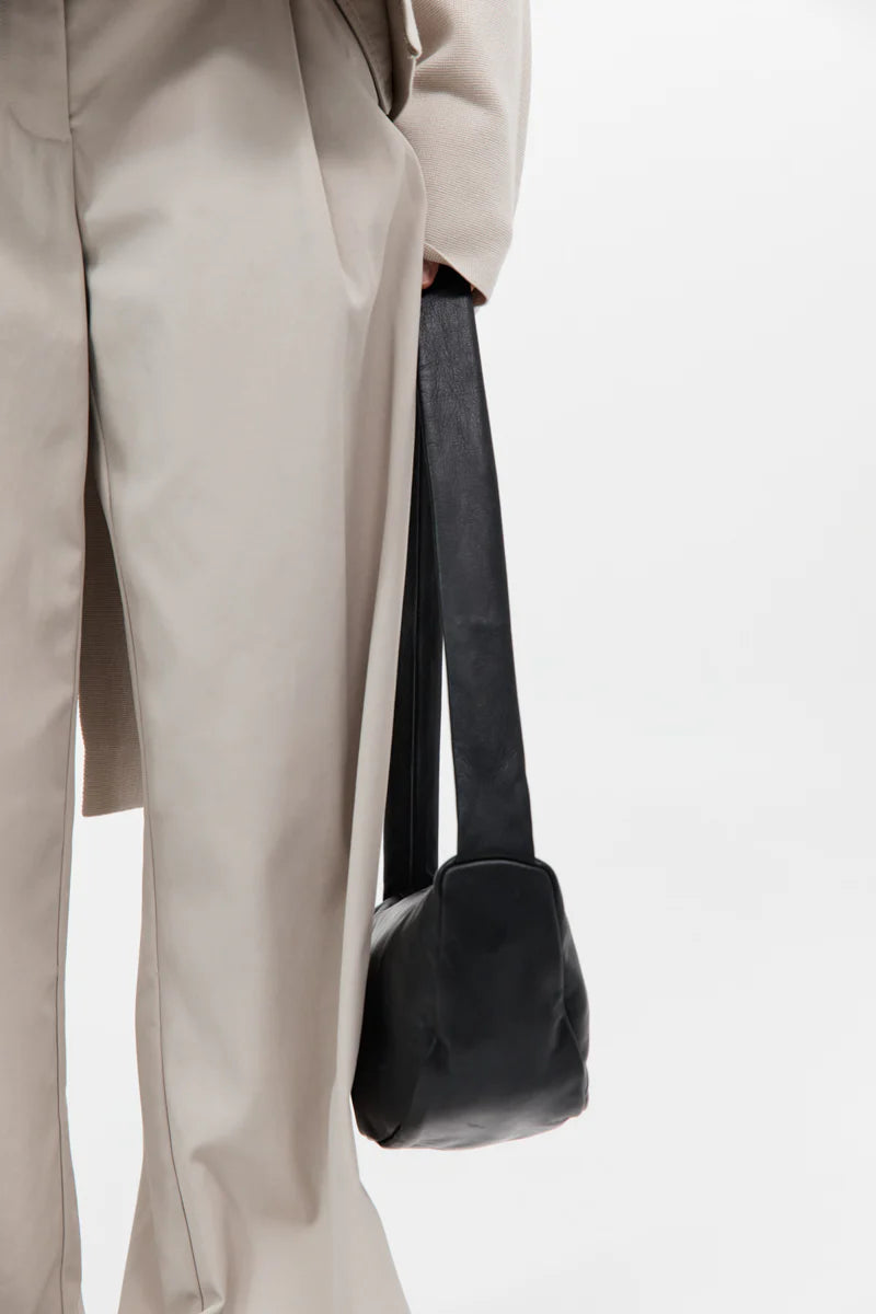 Person wearing a beige coat and holding a black bag on a white background