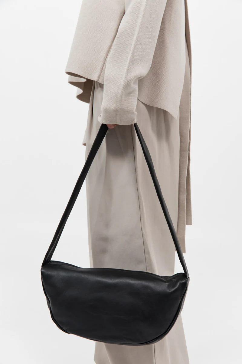 Black handbag held by a person wearing a beige coat on a white background