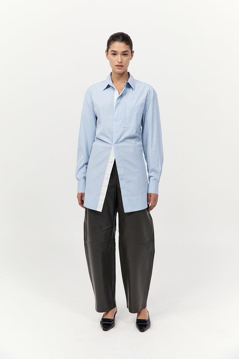 Person wearing a light blue striped shirt with black leather pants on a white background