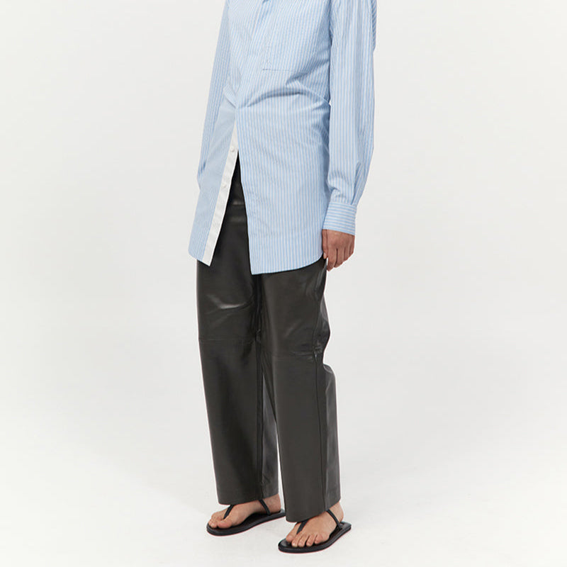 Person wearing a light blue pinstriped shirt and leather pants paired with minimal thong sandals 