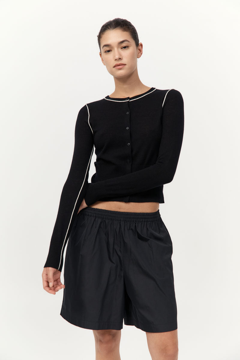 Person wearing a black long-sleeve top and black shorts on a white background