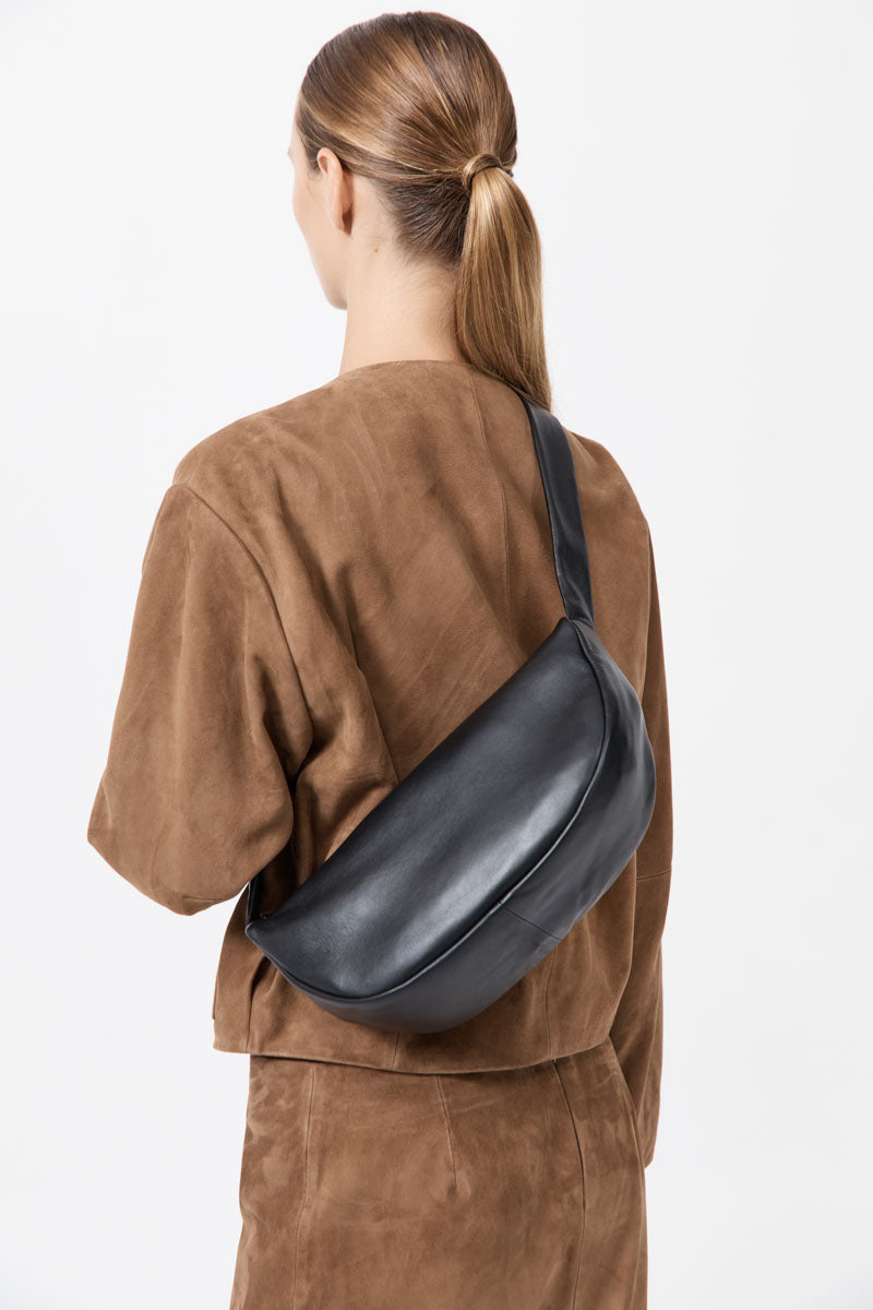 Person wearing a brown outfit with a black leather bag on a white background