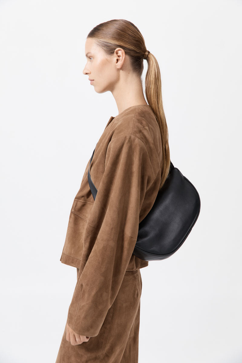 Person wearing a brown outfit with a black bag on a white background