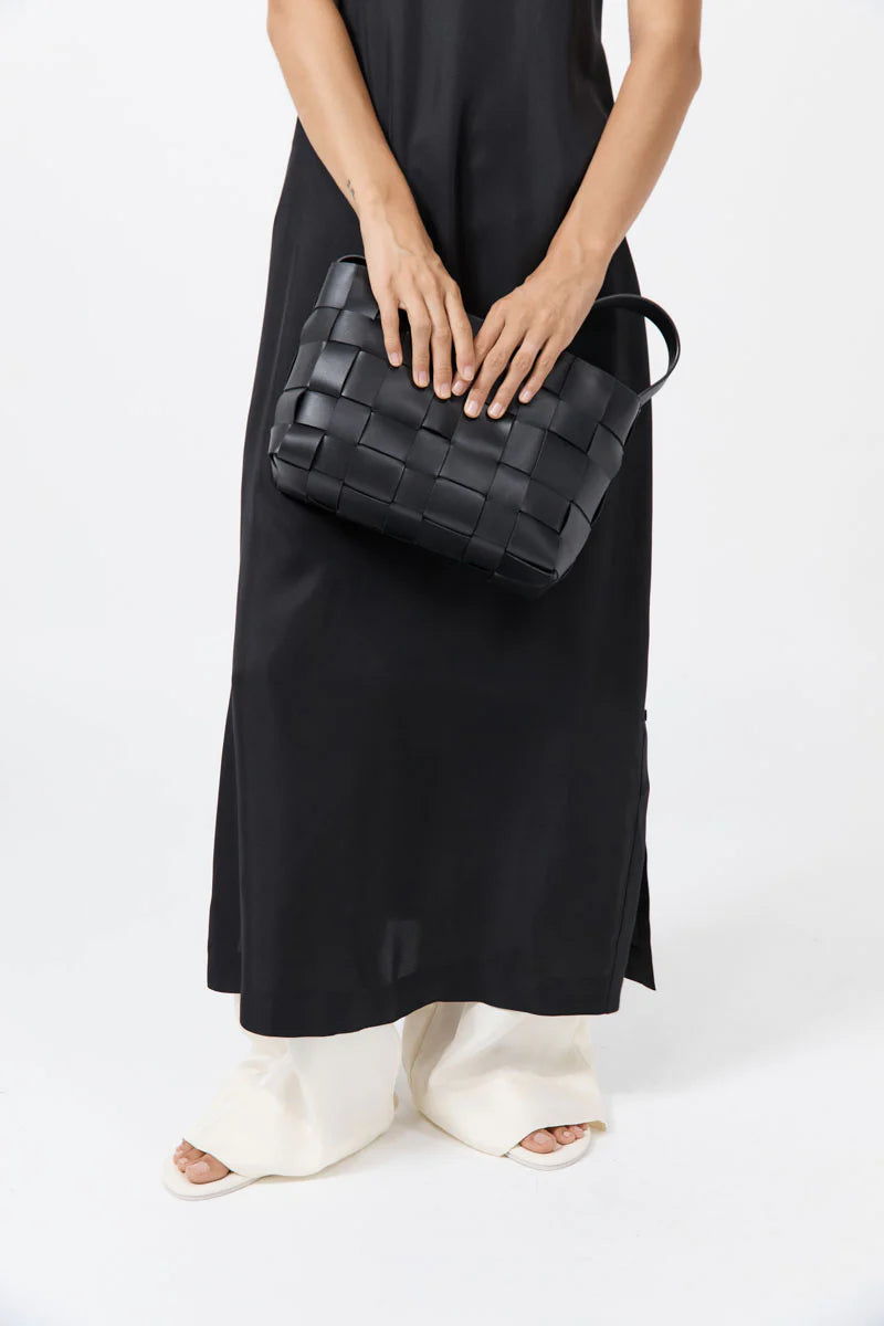 Person holding a black woven handbag against a white background