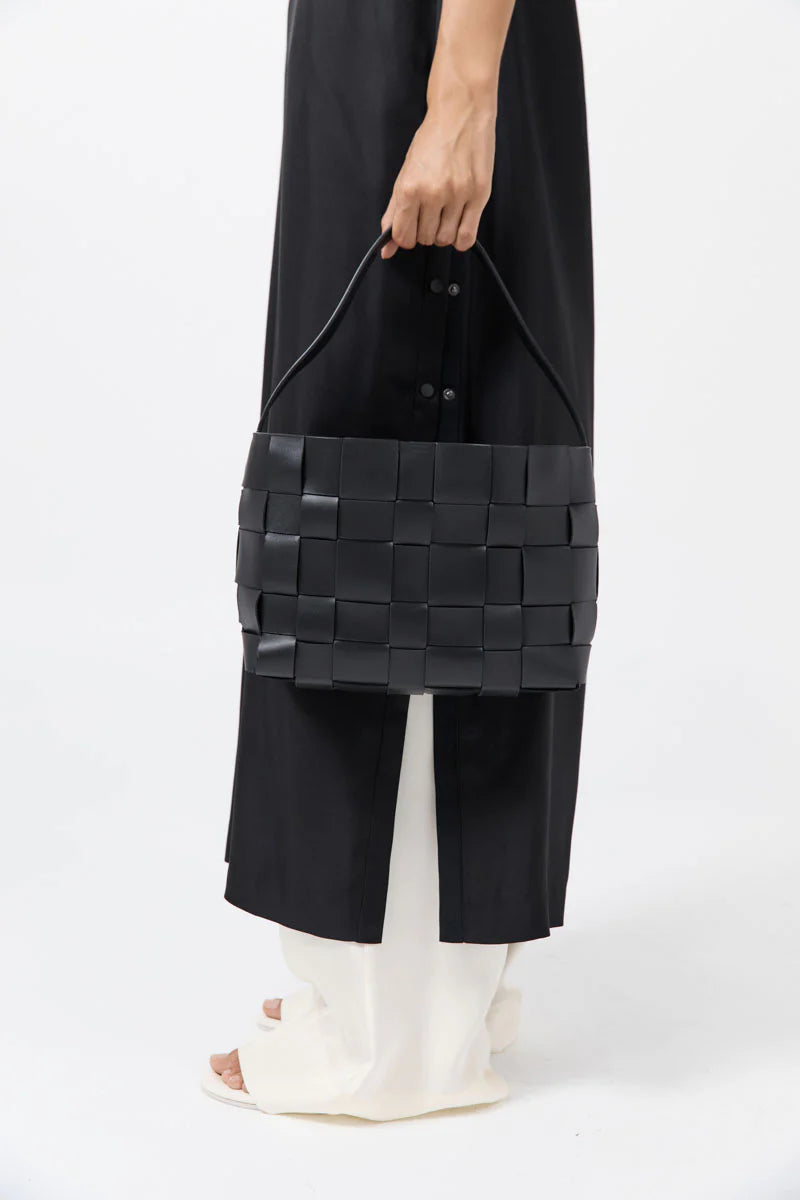 Person holding a black woven handbag against a white background