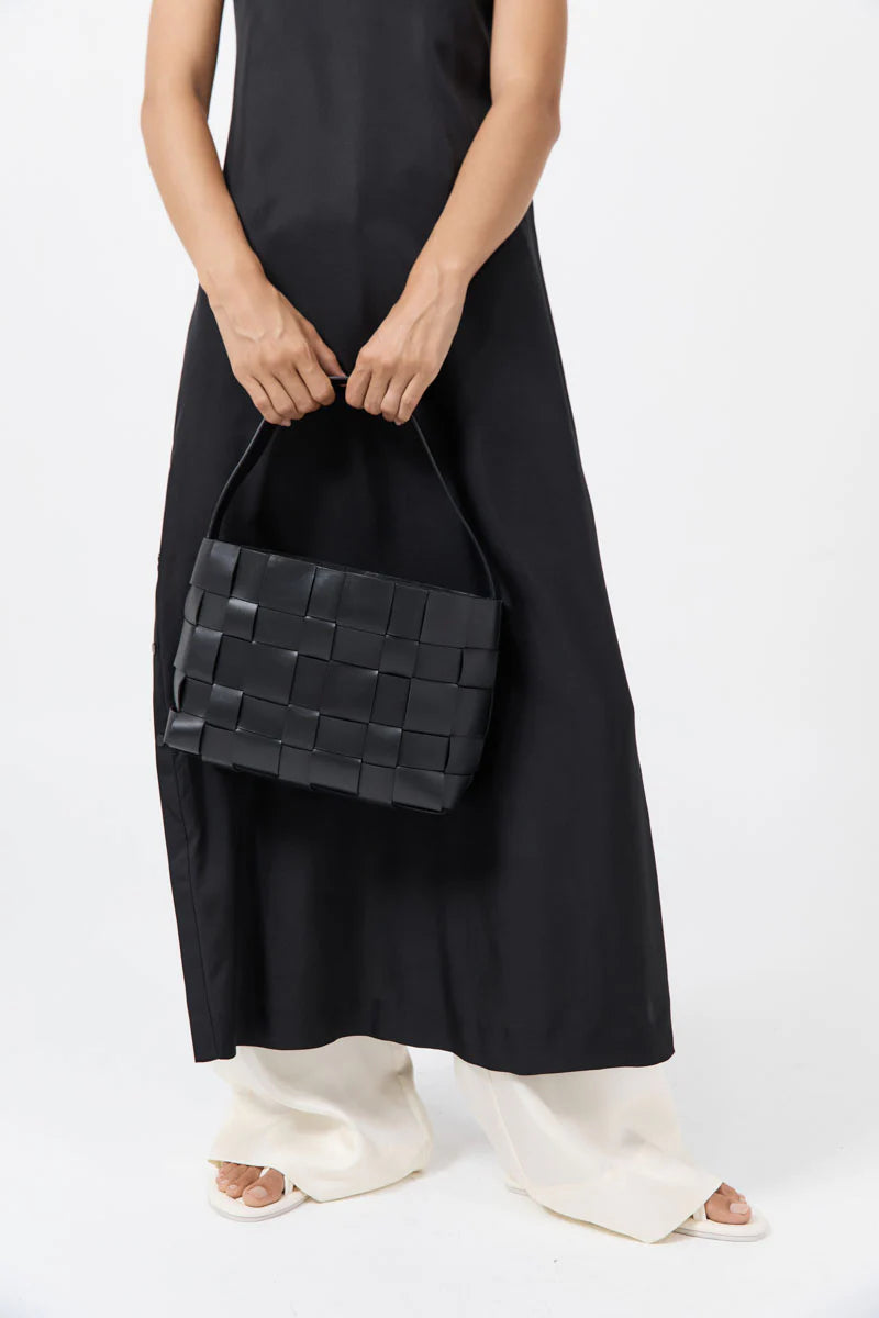 Person holding a woven black handbag against a white background