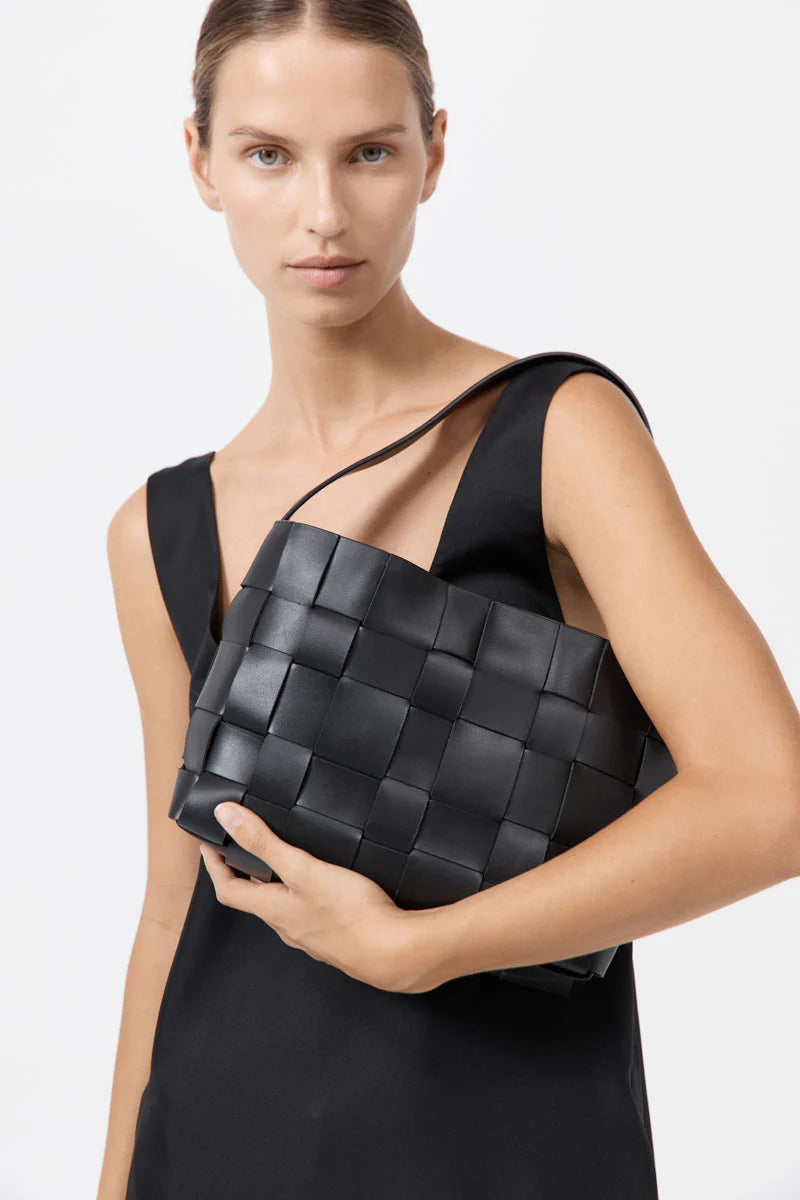Woman holding a black woven handbag against a white background