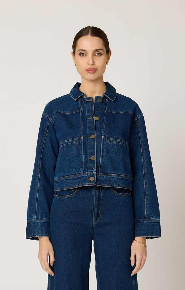 Woman wearing a blue denim jacket and pants on a plain background