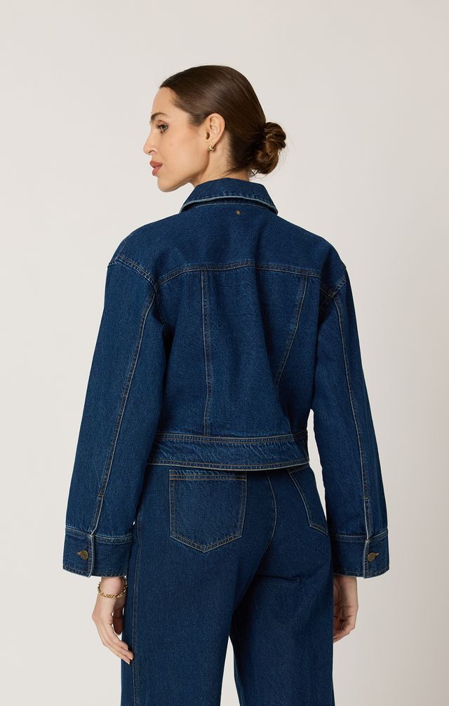 Woman wearing a blue denim jacket and pants on a light gray background