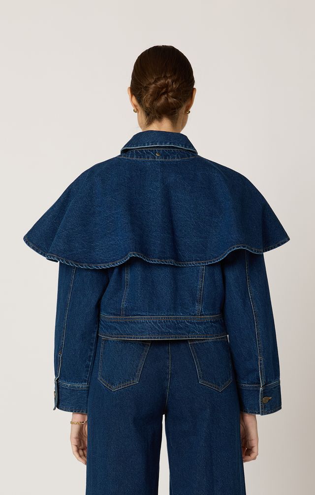 Person wearing a blue denim cape jacket and pants on a light gray background
