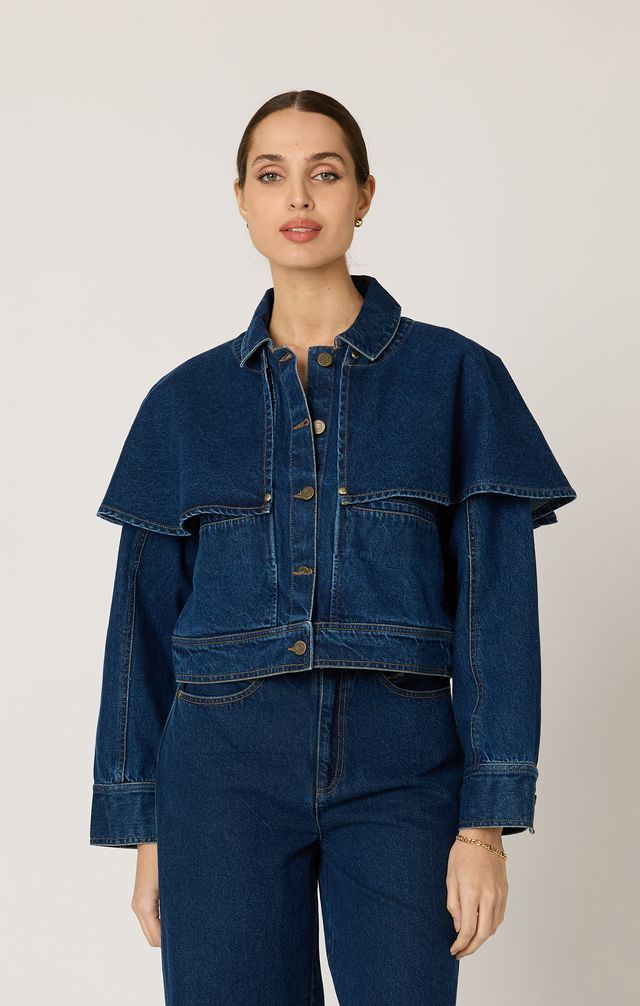 Person wearing a blue denim cape jacket and pants on a plain background