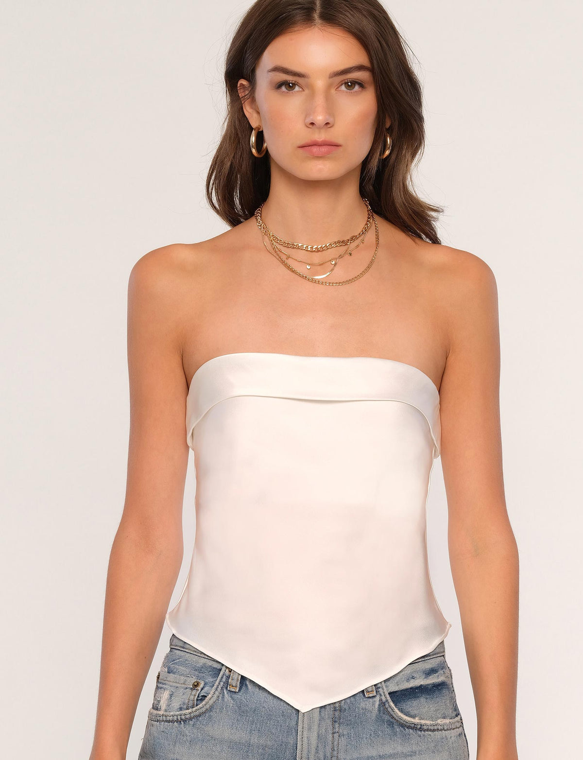 Woman wearing a white strapless top and blue jeans against a plain background.