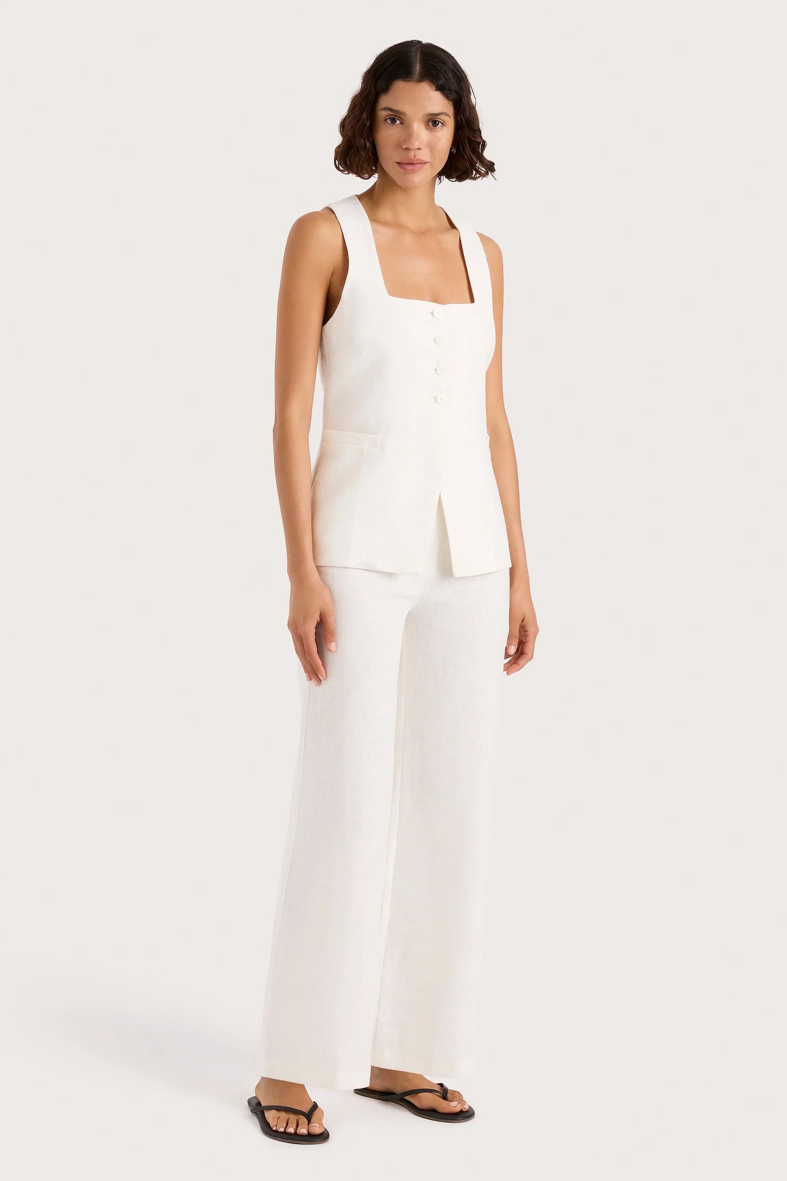 Woman wearing a white sleeveless top and pants on a white background