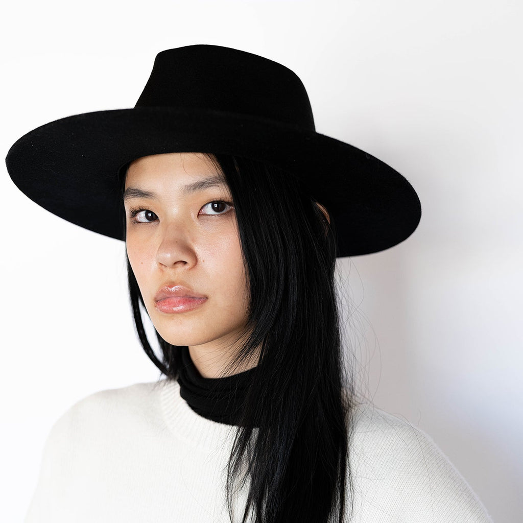 Woman wearing a black wide-brimmed hat and white sweater against a white background