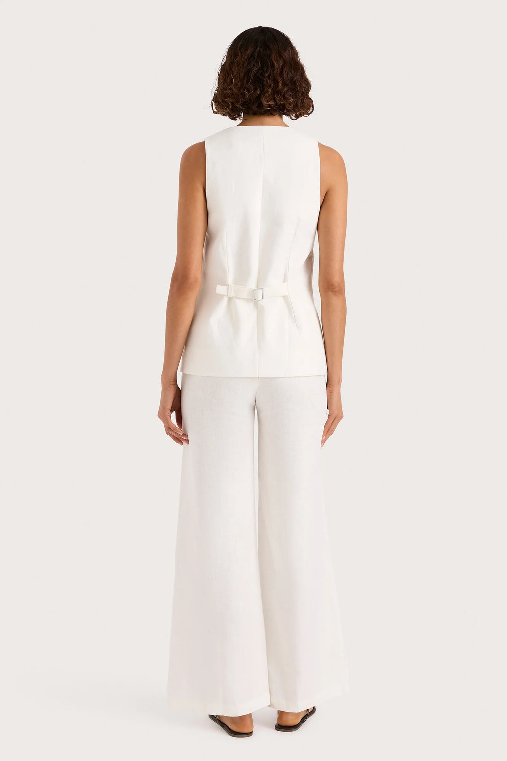 Woman wearing a white sleeveless top and pants set on a white background