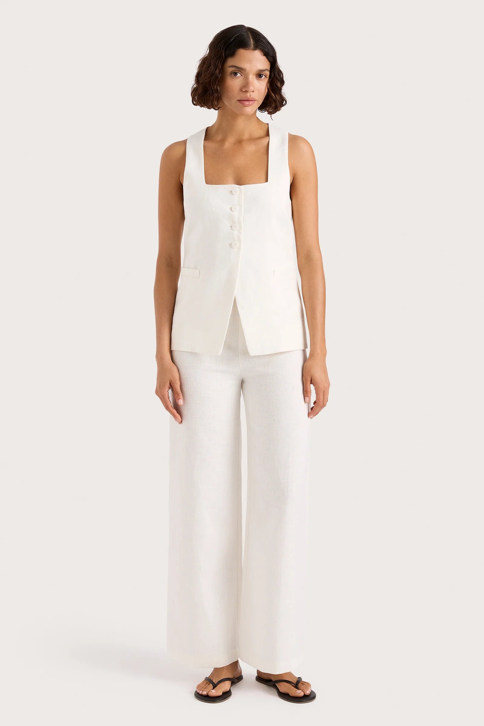 Woman wearing a white sleeveless top and wide-leg pants on a white background