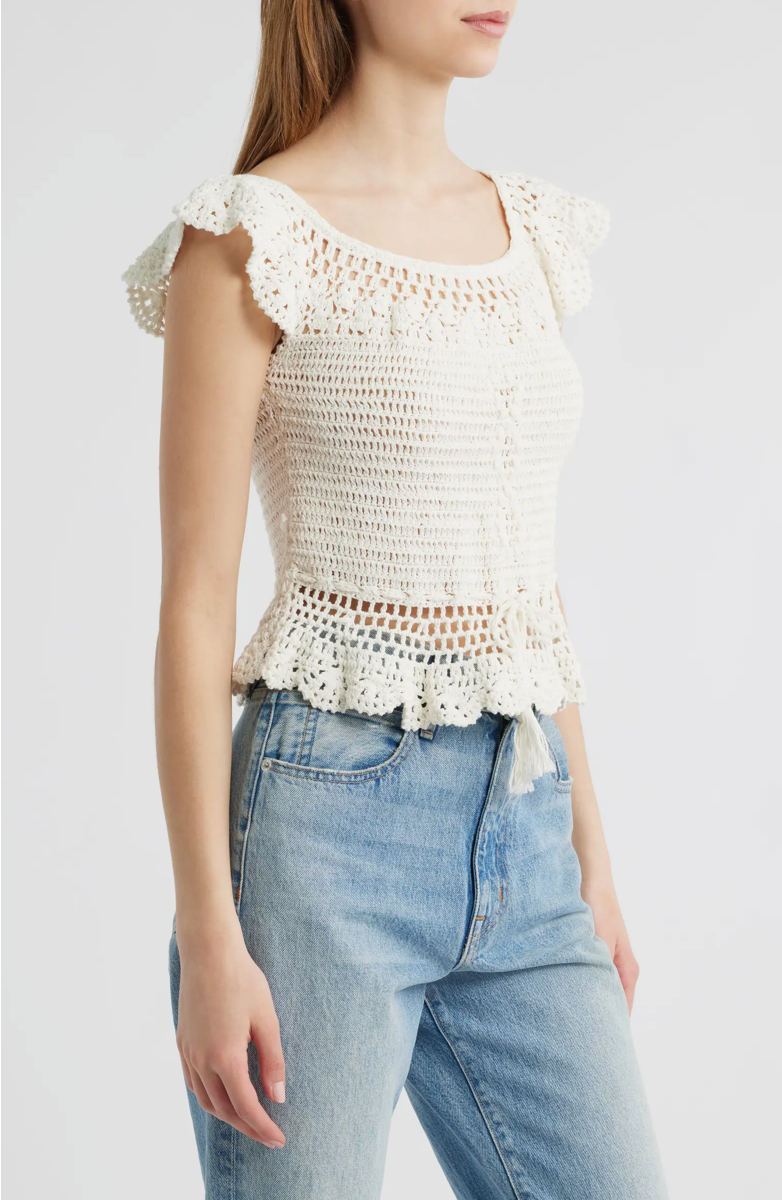 Woman wearing a white crochet top and blue jeans on a plain background.