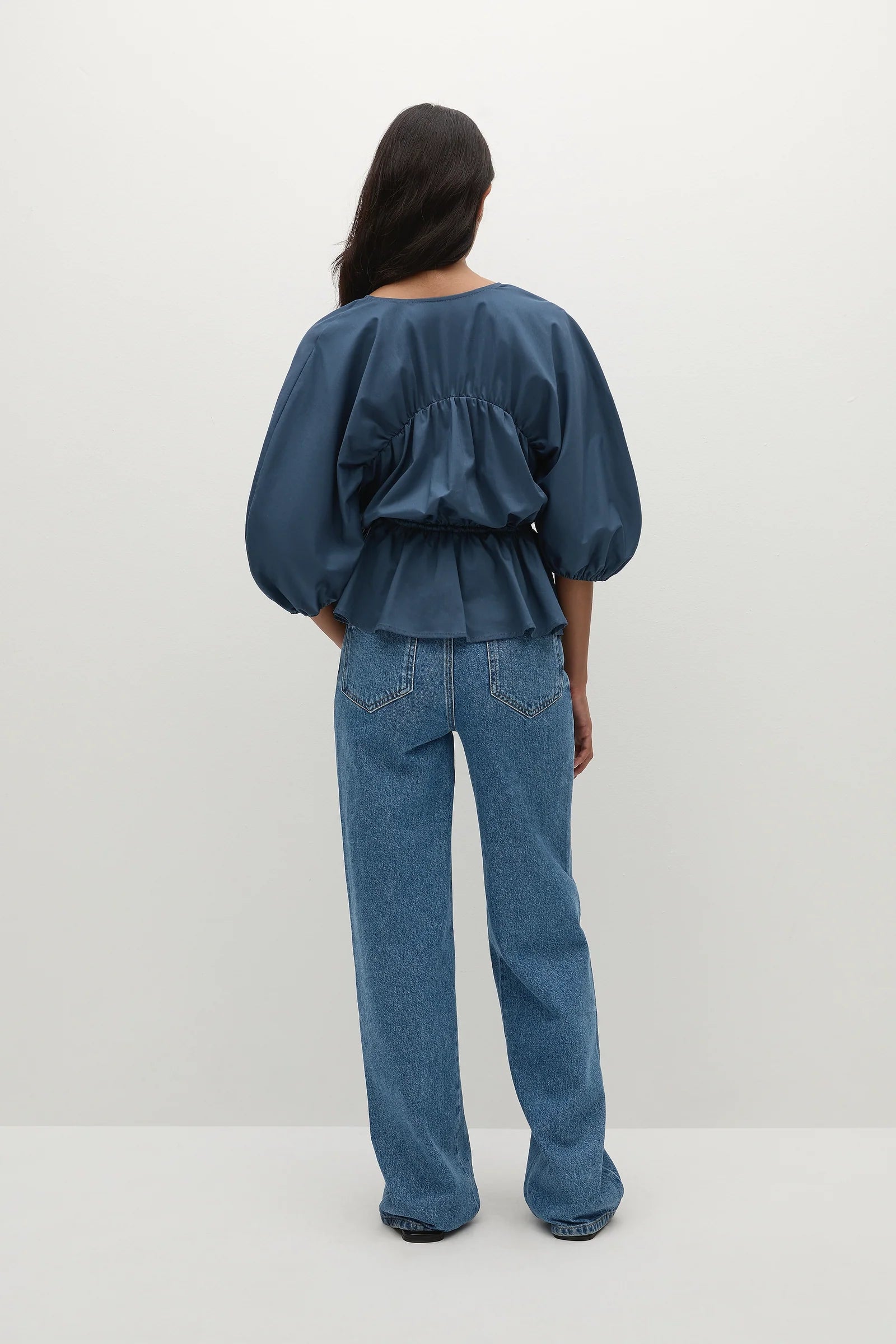 back view of a woman wearing a blue blouse paired with straight leg jeans