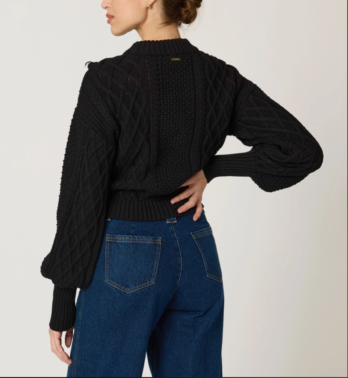 Person wearing a black ribbed sweater and blue jeans on a plain background