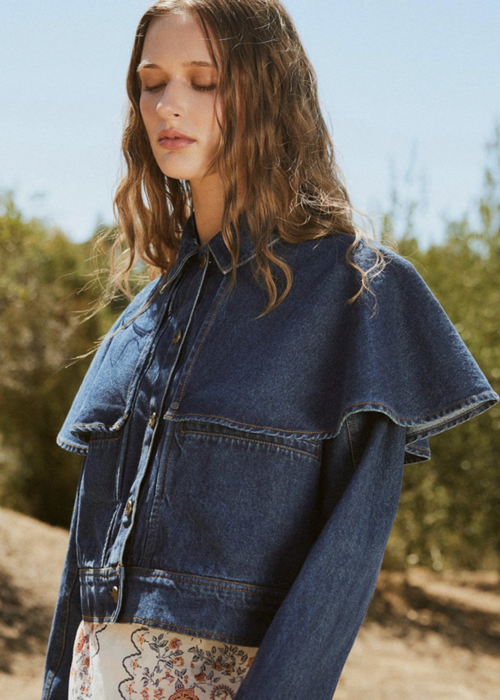 Woman wearing a denim jacket outdoors with greenery in the background