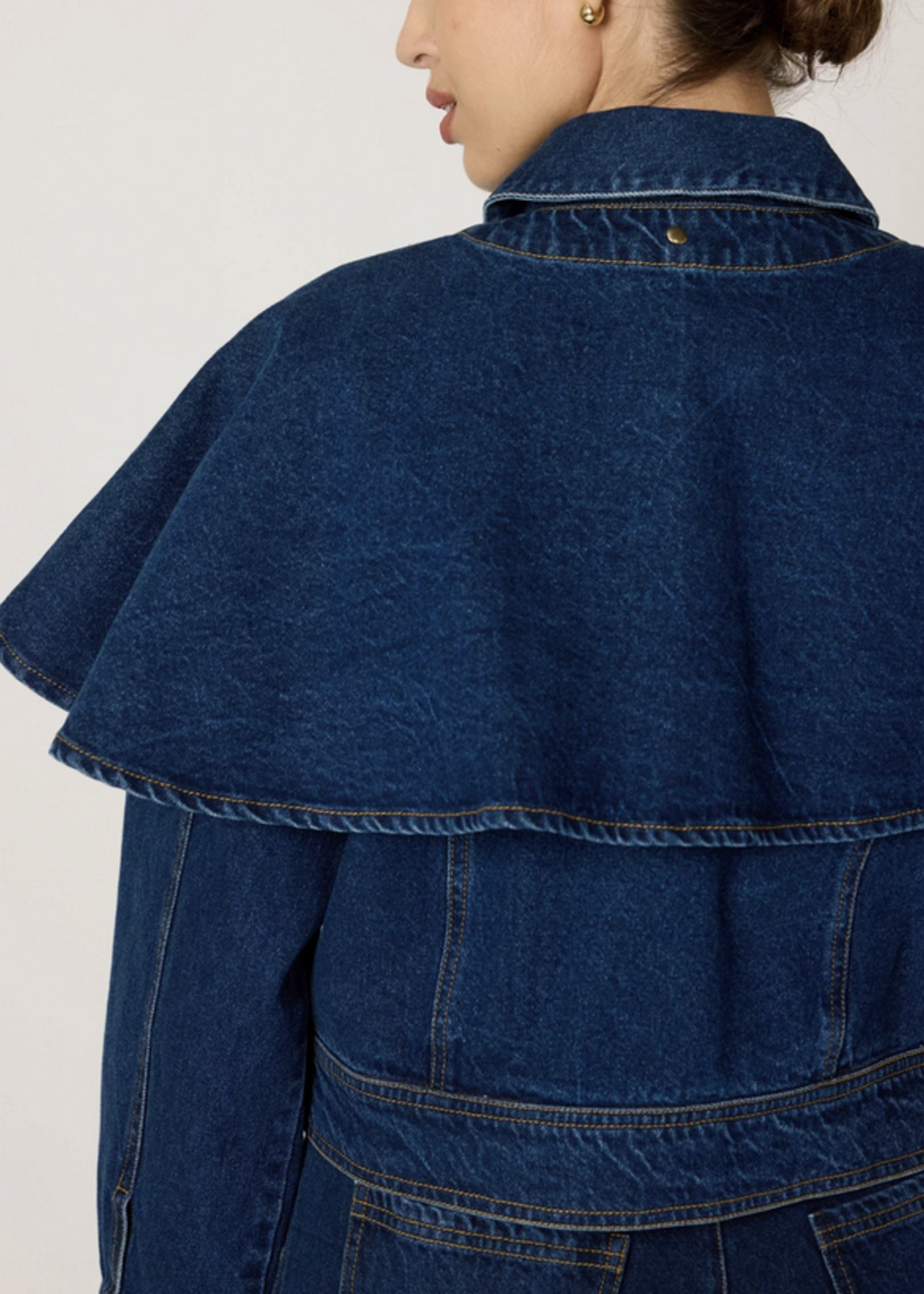 Blue denim jacket with a cape worn by a person on a white background