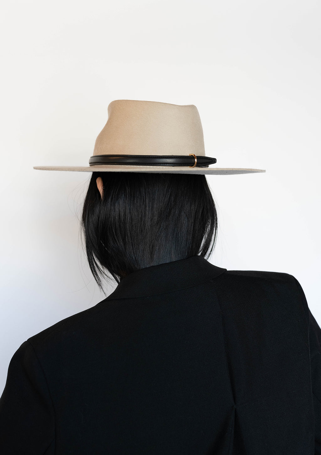 Person wearing a beige fedora hat with a black band on a white background